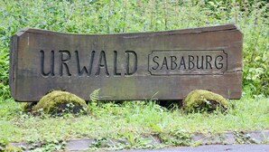Une pancarte en bois portant l’inscription « URWALD SABABURG », entourée de verdure.