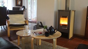 Un salon chaleureux avec une cheminée, un fauteuil confortable, une petite table avec une théière et un verre, et un magazine.