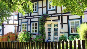 Une maison traditionnelle à colombages, avec une clôture en bois, une porte à deux battants et une fenêtre agrémentée d’une jardinière.