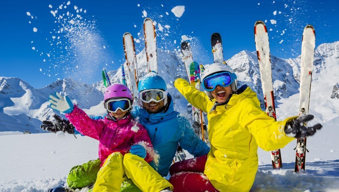 Three people in colorful winter clothing with skis in the background.