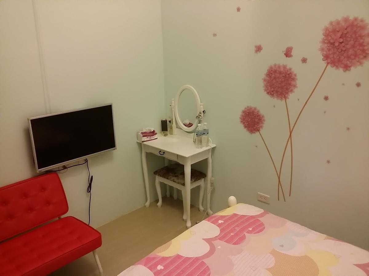 A bedroom with a TV, a desk with a mirror, a red chair, and a bed with a floral bedspread.