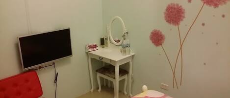 A bedroom with a TV, a desk with a mirror, a red chair, and a bed with a floral bedspread.