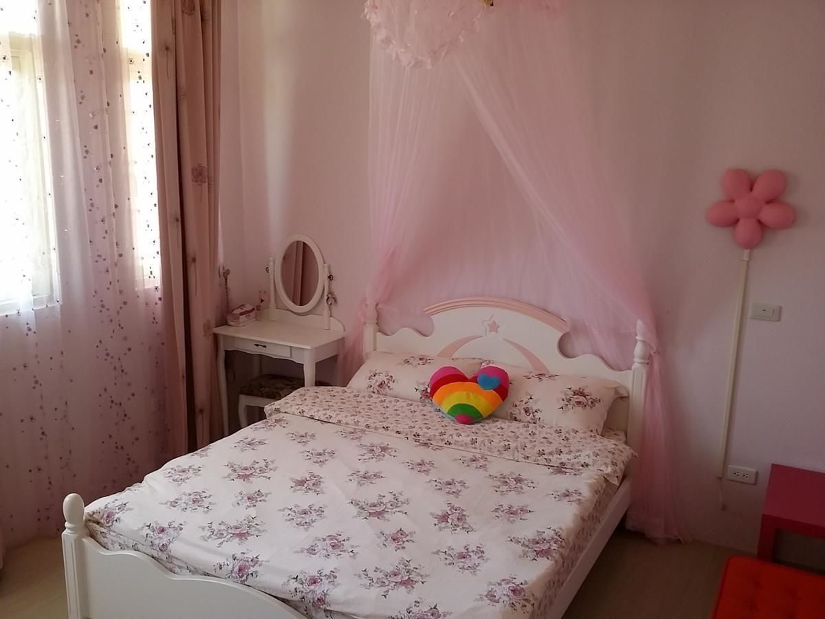 A bedroom with a bed, a bedside table, a mirror, and a pink flower decoration.
