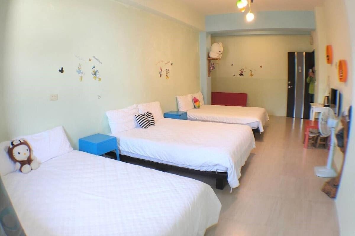 A hotel room with three beds, a blue nightstand, and a red chair.