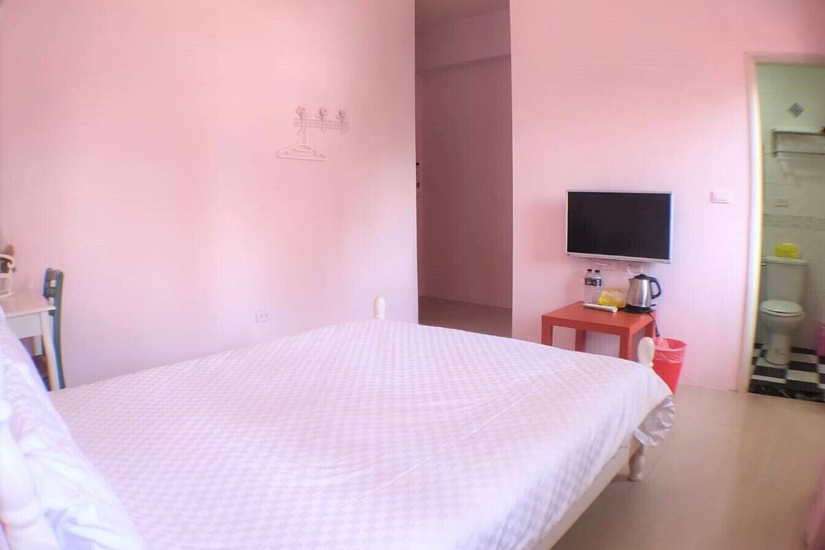 A bedroom with a bed, a TV, a small table with a kettle, and a red trash bin.