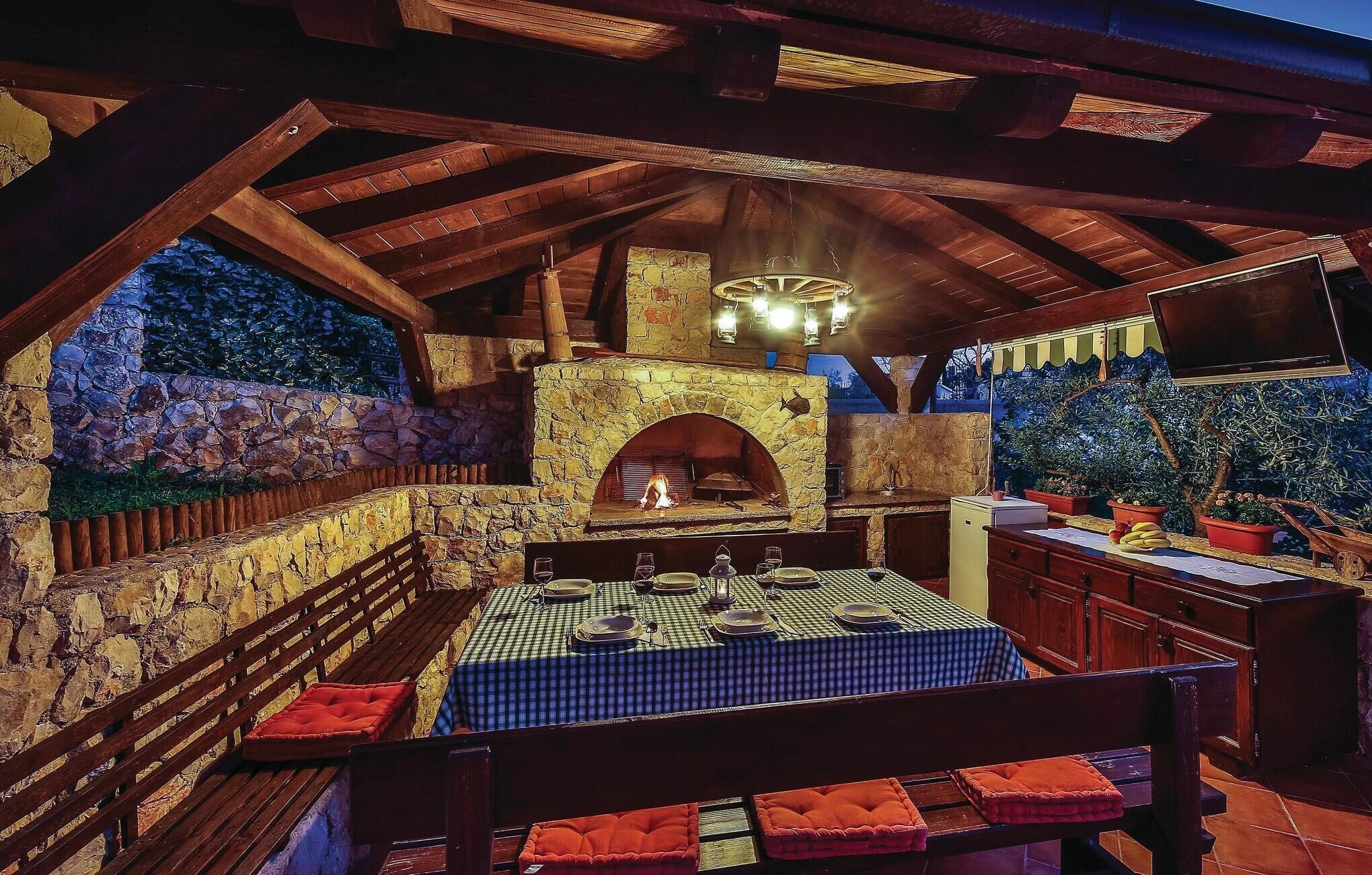 An outdoor kitchen area with a stone fireplace, wooden beams, and a dining table set for four.