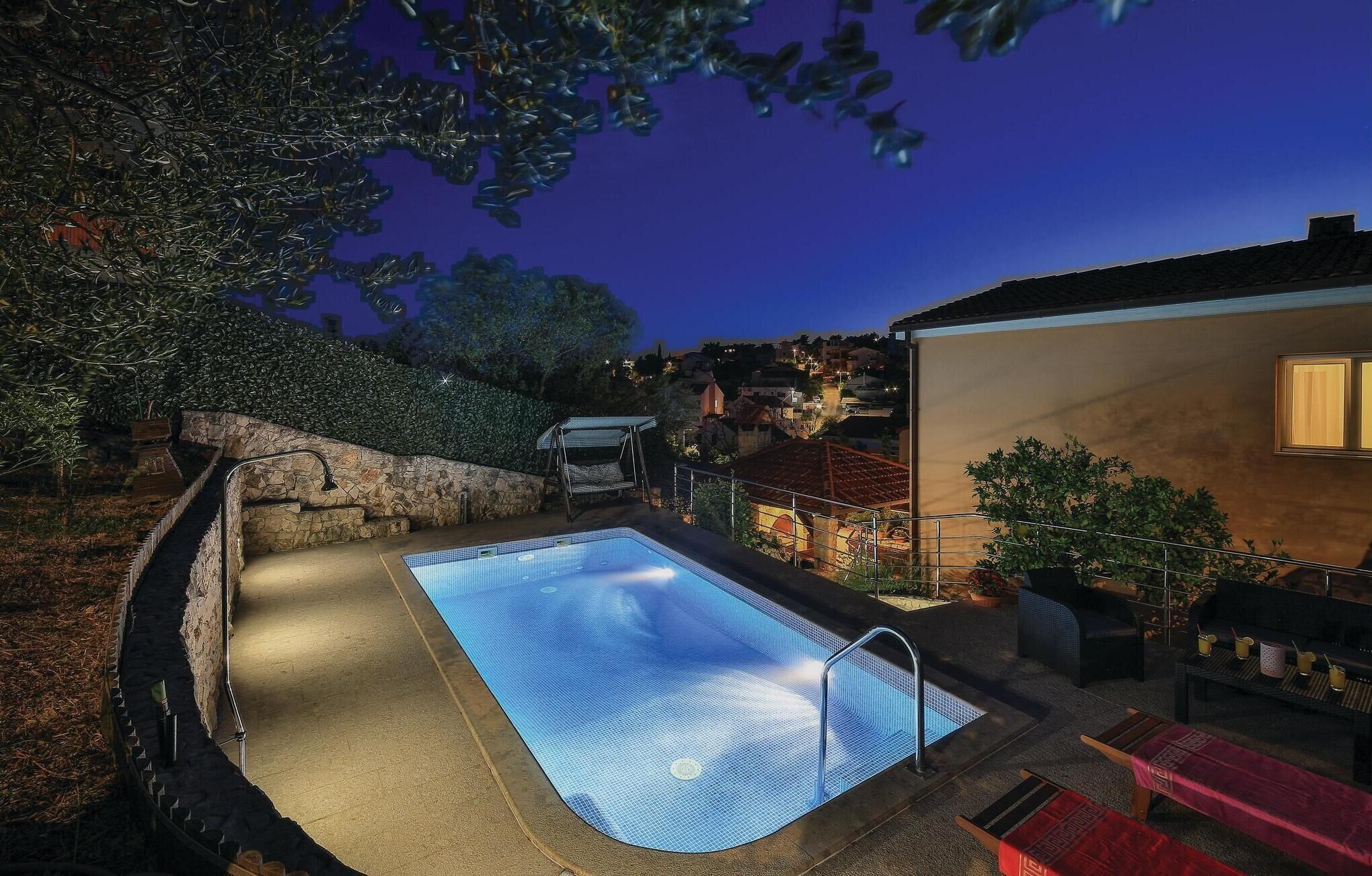 A swimming pool with a stone wall and a view of a town at dusk.