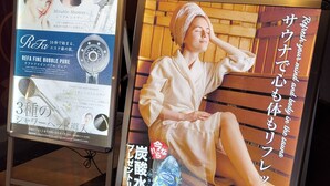 Un cartel con una mujer en bata, un letrero de ReFa Fine Bubble Pure y una pared de madera al fondo.