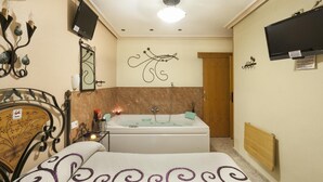 A bedroom with a bed, a bathroom with a bathtub, a TV mounted on the wall, and a ceiling light. - Pensión San José (Bullas)