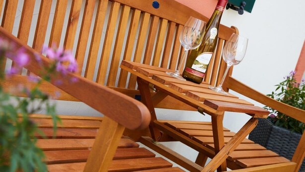 A wooden outdoor seating area with a table and chairs, a bottle of wine, and a glass. - Mosel - Bernkastel-Kues - Holiday House "Half-timbered house with charm"  (Bernkastel-Kues)