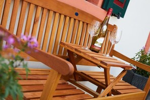 A wooden outdoor seating area with a table and chairs, a bottle of wine, and a glass.