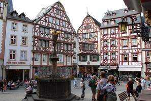 A traditional European town square with half-timbered buildings, a central fountain, and outdoor seating areas.