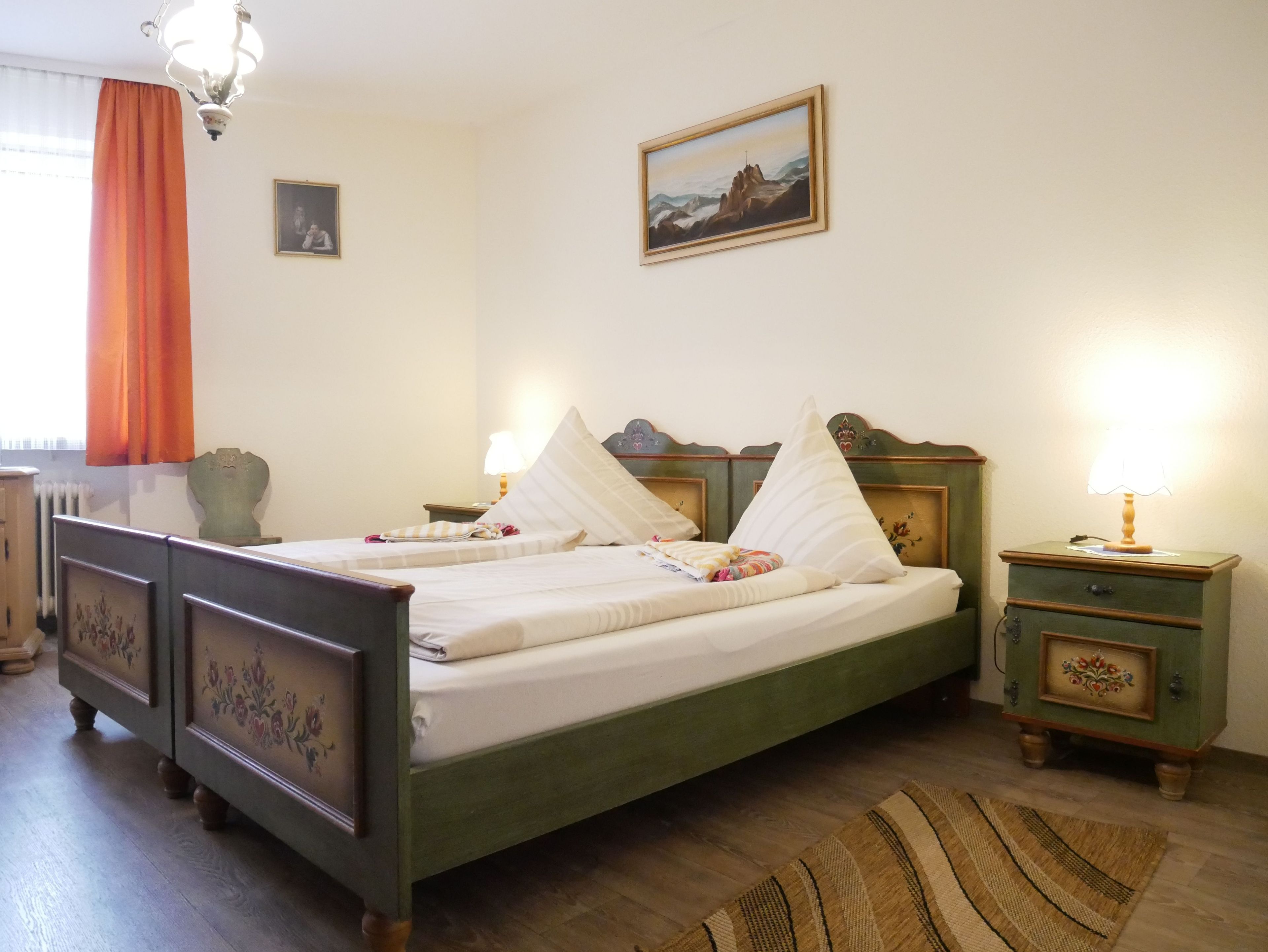 Un dormitorio con cama, mesitas de noche, lámpara, un cuadro y una ventana con cortinas.