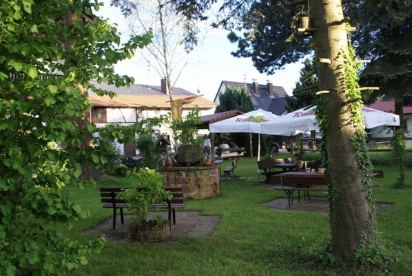 An outdoor seating area with stone tables and benches, surrounded by greenery and trees.