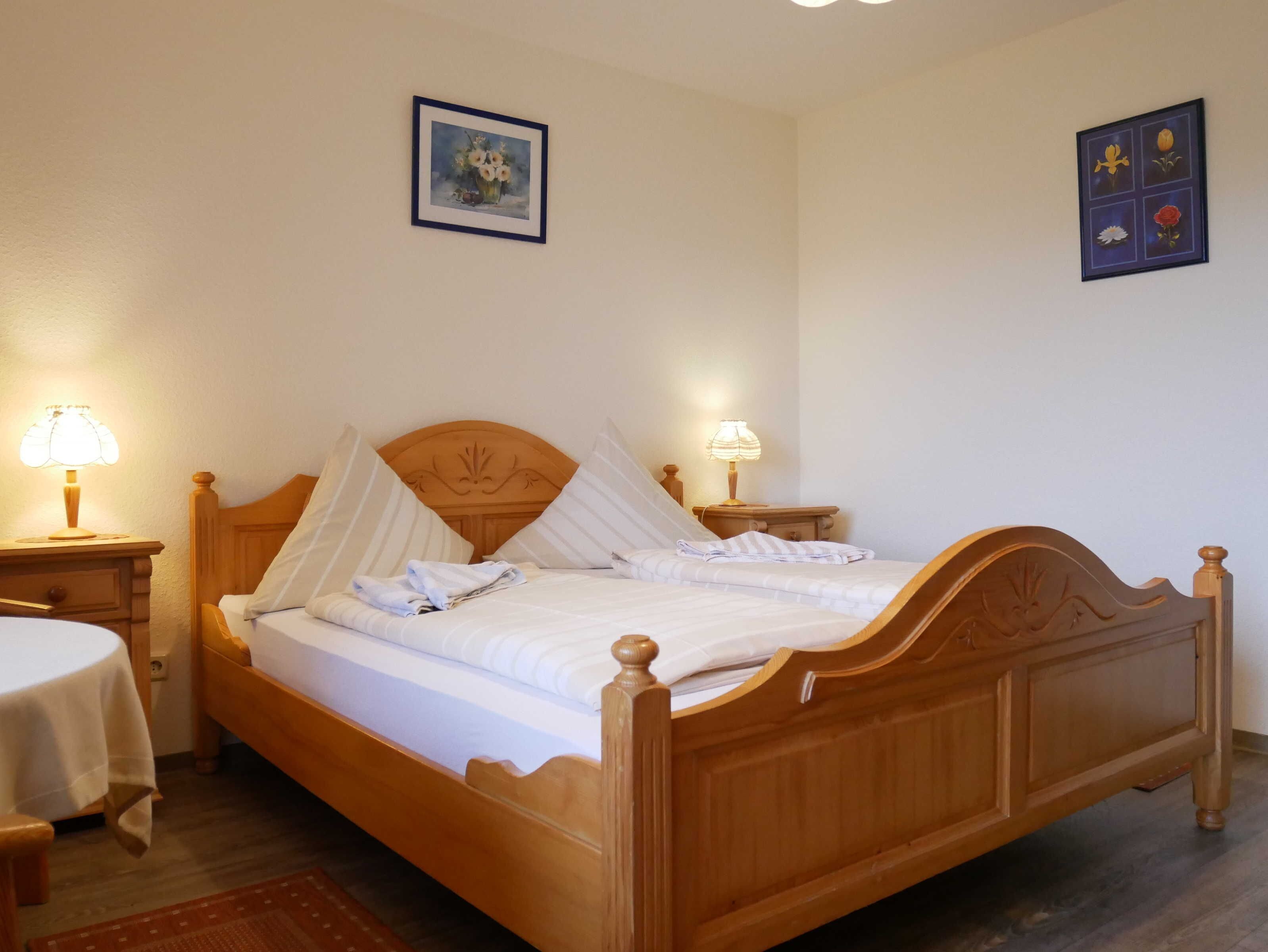 A wooden bed with a canopy, two bedside lamps, a small table with a lamp, and a framed picture on the wall.