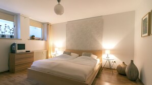 Ein modernes Schlafzimmer mit einem großen Bett, Nachttischlampen, einem Schminktisch, einem Fernseher und dekorativen Vasen.