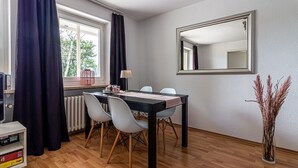 Ein Essbereich mit Tisch, Stühlen, einem Spiegel und einer Vase mit Trockenpflanzen.