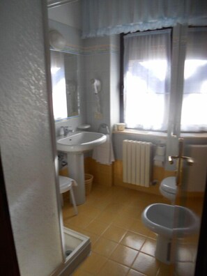 A bathroom with a sink, toilet, and bidet. There is a window with curtains and a radiator. - Albergo Generale Cantore (Abbadia San Salvatore)