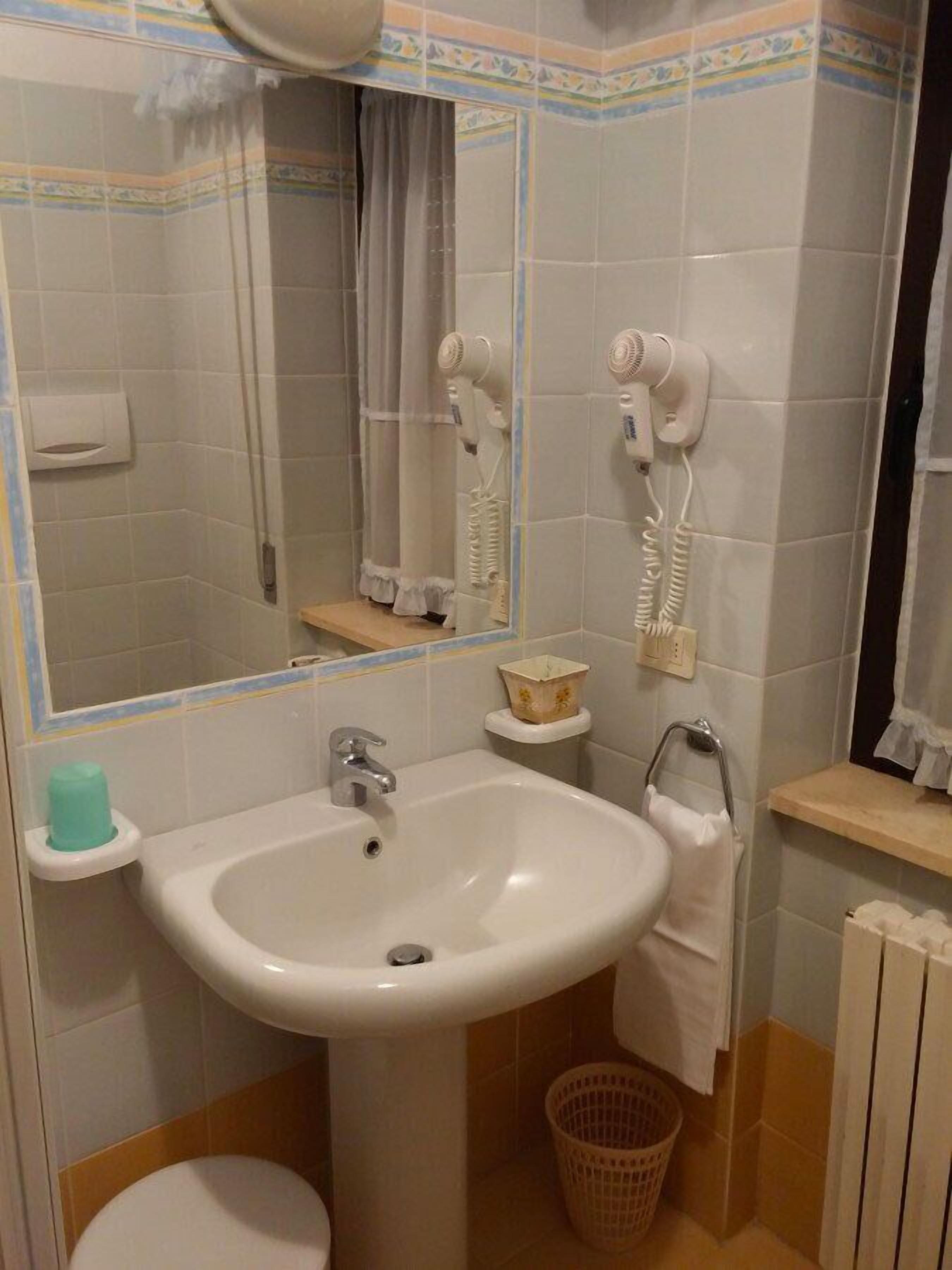 A bathroom with a sink, mirror, hairdryer, and a small shelf with a basket.