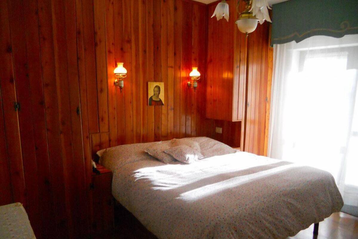 A wooden room with a bed, two wall-mounted lamps, and a framed picture on the wall.