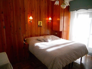 Quarto de madeira com uma cama, duas luminárias na parede e um quadro emoldurado.