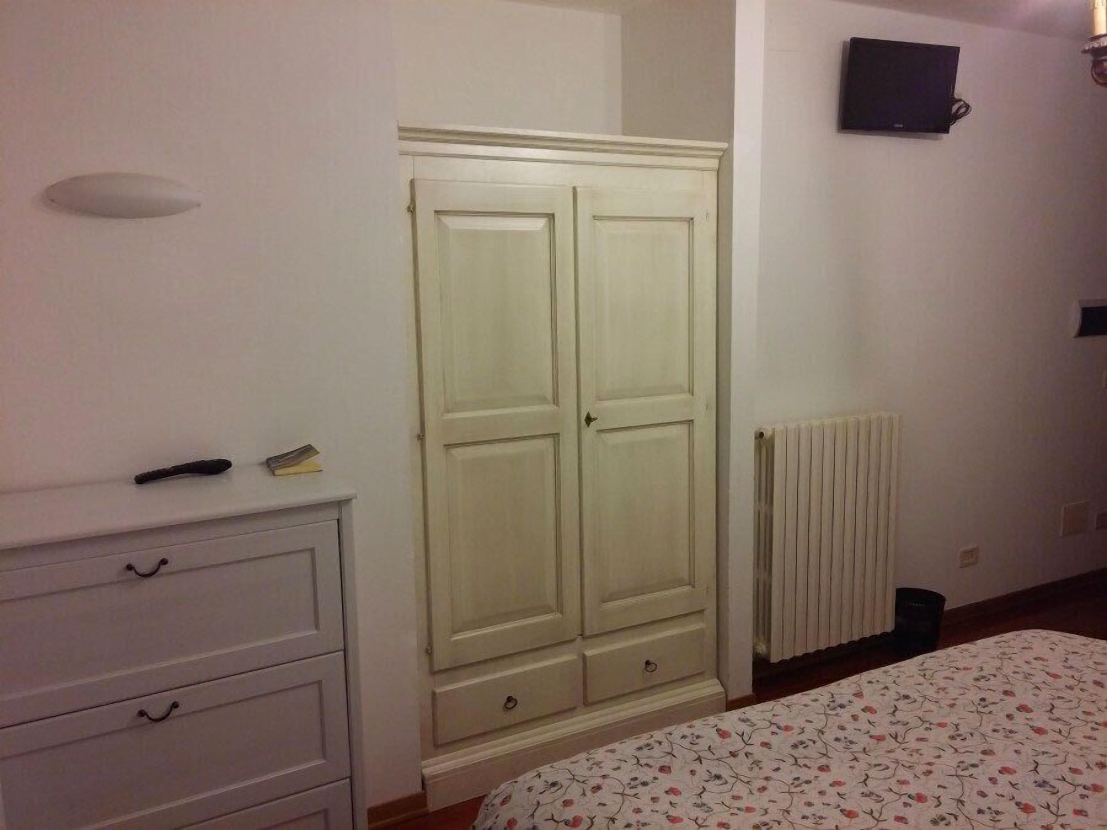 A bedroom with a bed, a wardrobe, a radiator, and a TV on the wall.