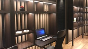A modern office space with a laptop on a desk, a chair, and a bookshelf with a vase of flowers. - New Tomakomai Prince Hotel Nagomi (Tomakomai)