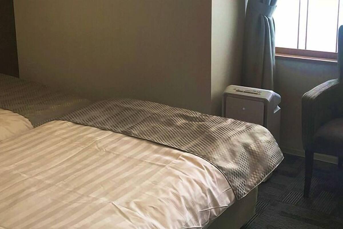 A hotel room with two beds, a radiator, and a chair.
