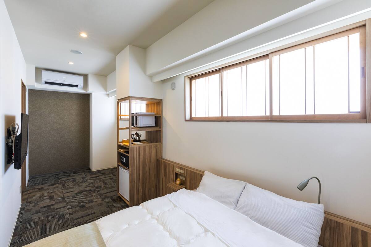 A hotel room with a bed, a desk with a chair, a microwave, and a small cabinet.