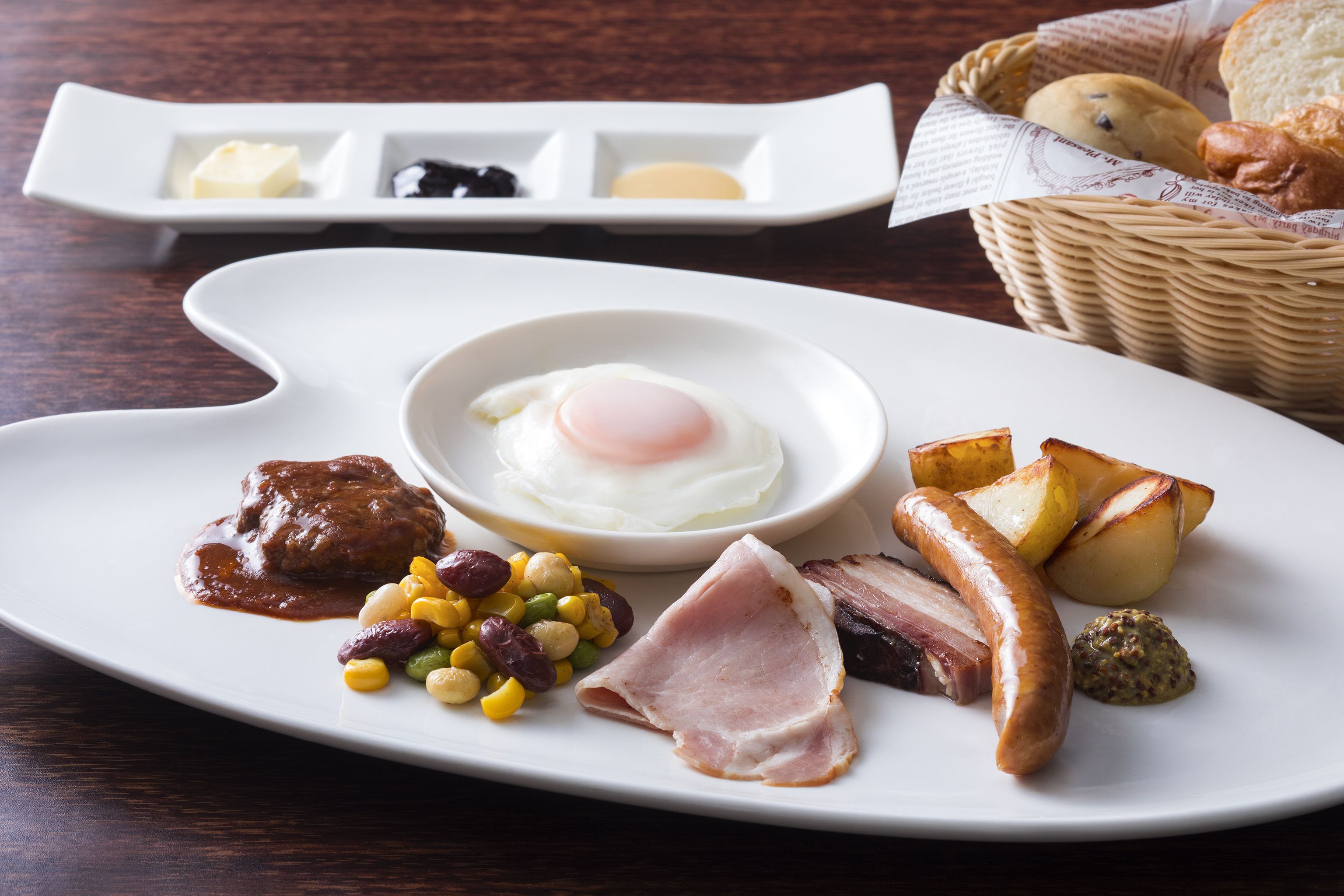 A breakfast plate with eggs, sausages, ham, beans, and potatoes.