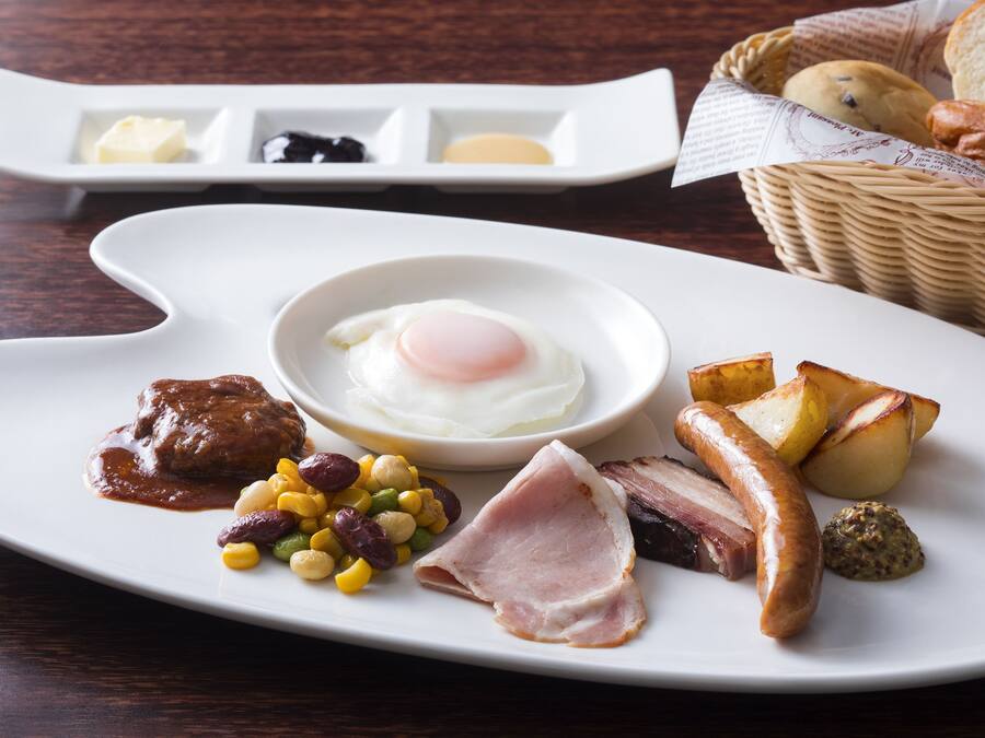A breakfast plate with eggs, sausages, ham, beans, and potatoes.