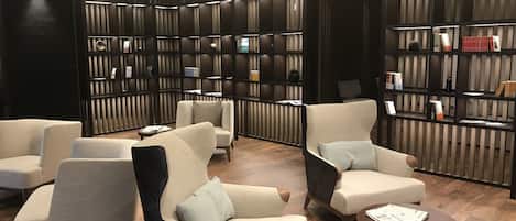Un espacio lounge moderno con sofás y sillones, estanterías de madera y una mesa redonda con periódicos.