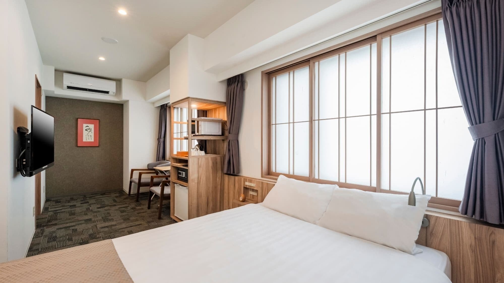 Una habitación de hotel con cama, escritorio, televisor y un ventanal con cortinas.
