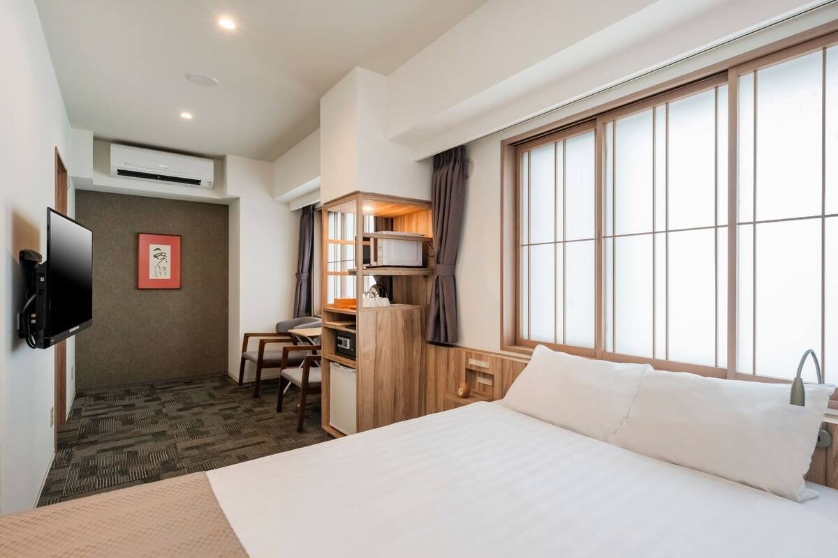 A hotel room with a bed, a desk, a TV, and a large window with curtains.