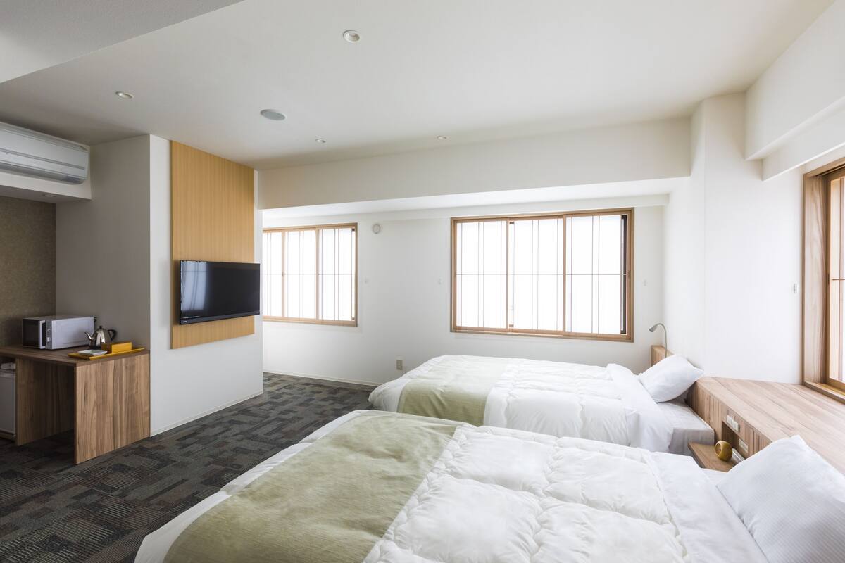 A hotel room with two beds, a TV, a desk with a microwave, and large windows.
