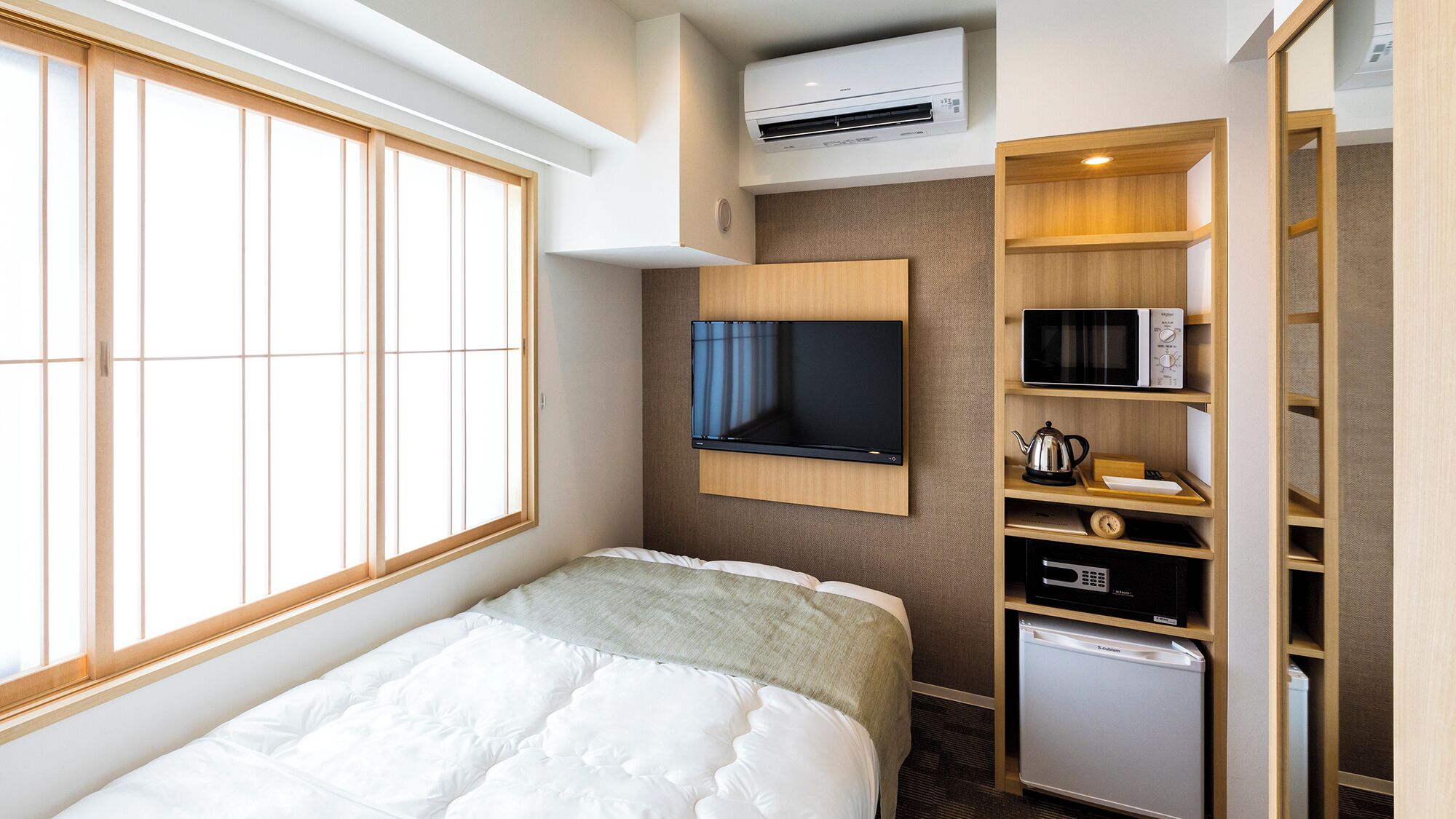Habitación de hotel con cama, televisión montada en la pared, microondas, refrigerador y ventana con persianas.