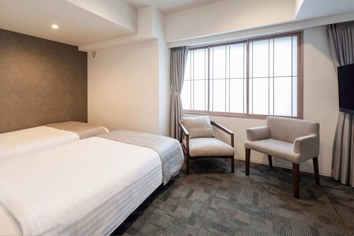 A hotel room with two beds, a chair, a TV, and a large window.