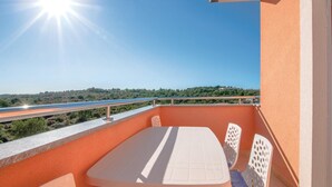 Un balcon avec une table et des chaises, une balustrade et une vue sur une route et des espaces verts.