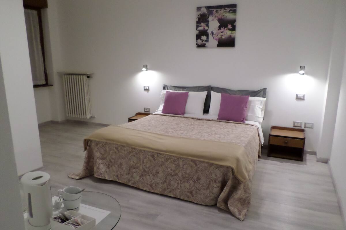 A bedroom with a bed, bedside tables, a radiator, and a wall-mounted artwork.