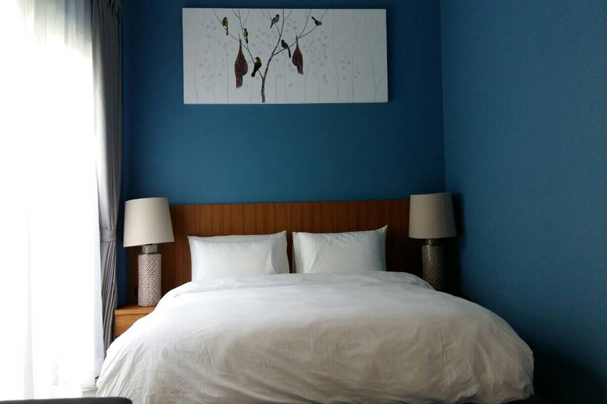 A neatly made bed with white linens, a wooden headboard, and two bedside lamps on either side.