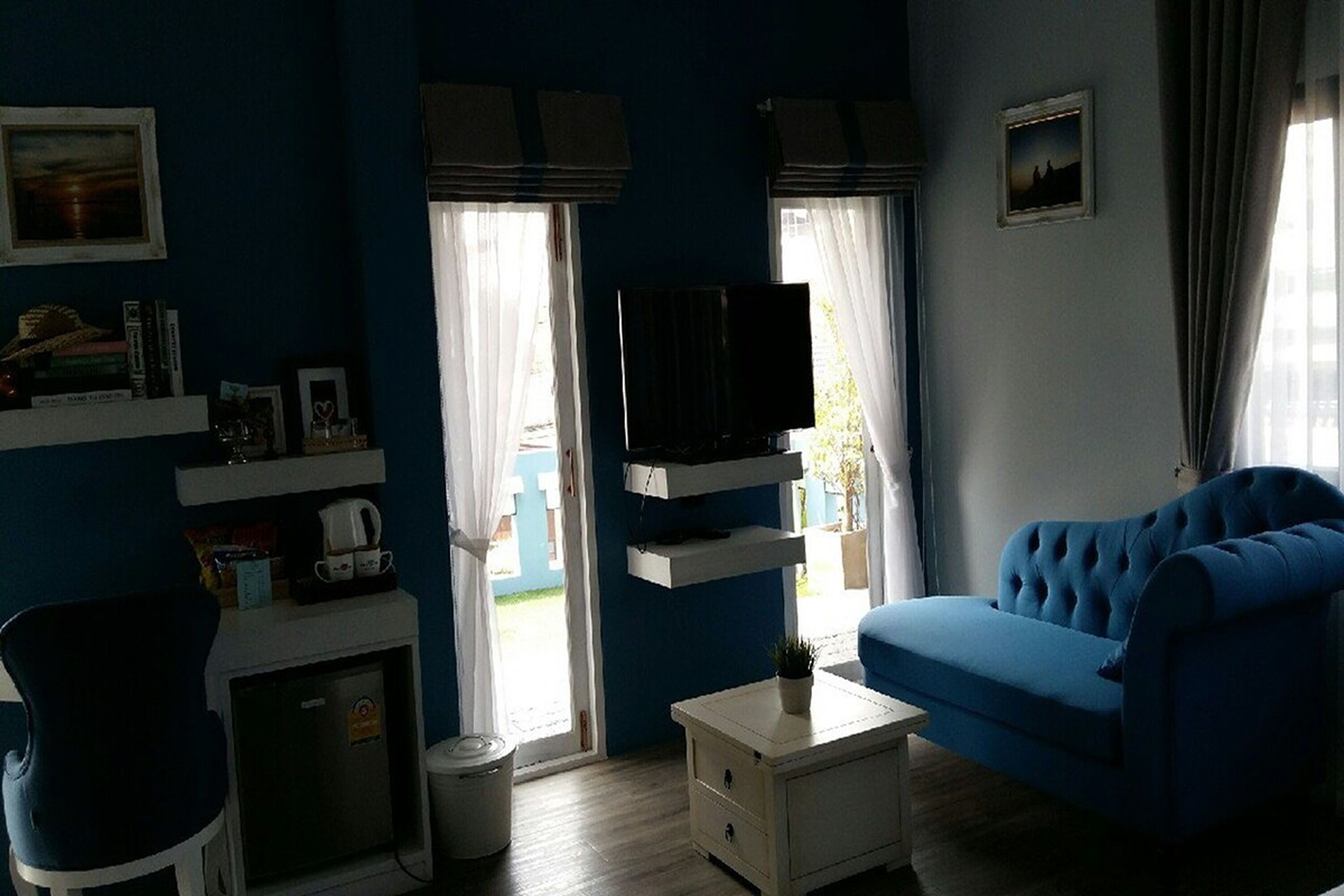 Un salon avec un canapé bleu, un téléviseur posé sur un meuble, une petite table et une bibliothèque.