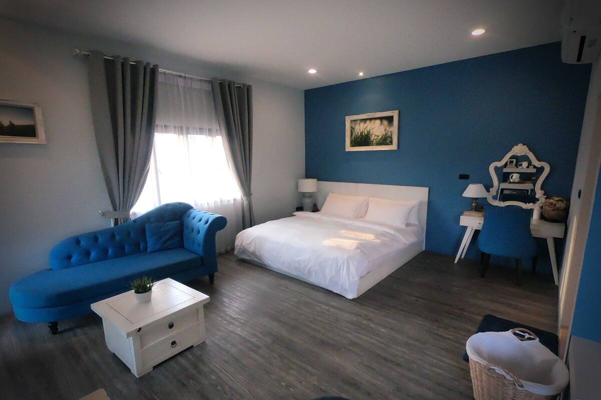 A room with a bed, a blue sofa, a small white table, a lamp, and a picture on the wall.