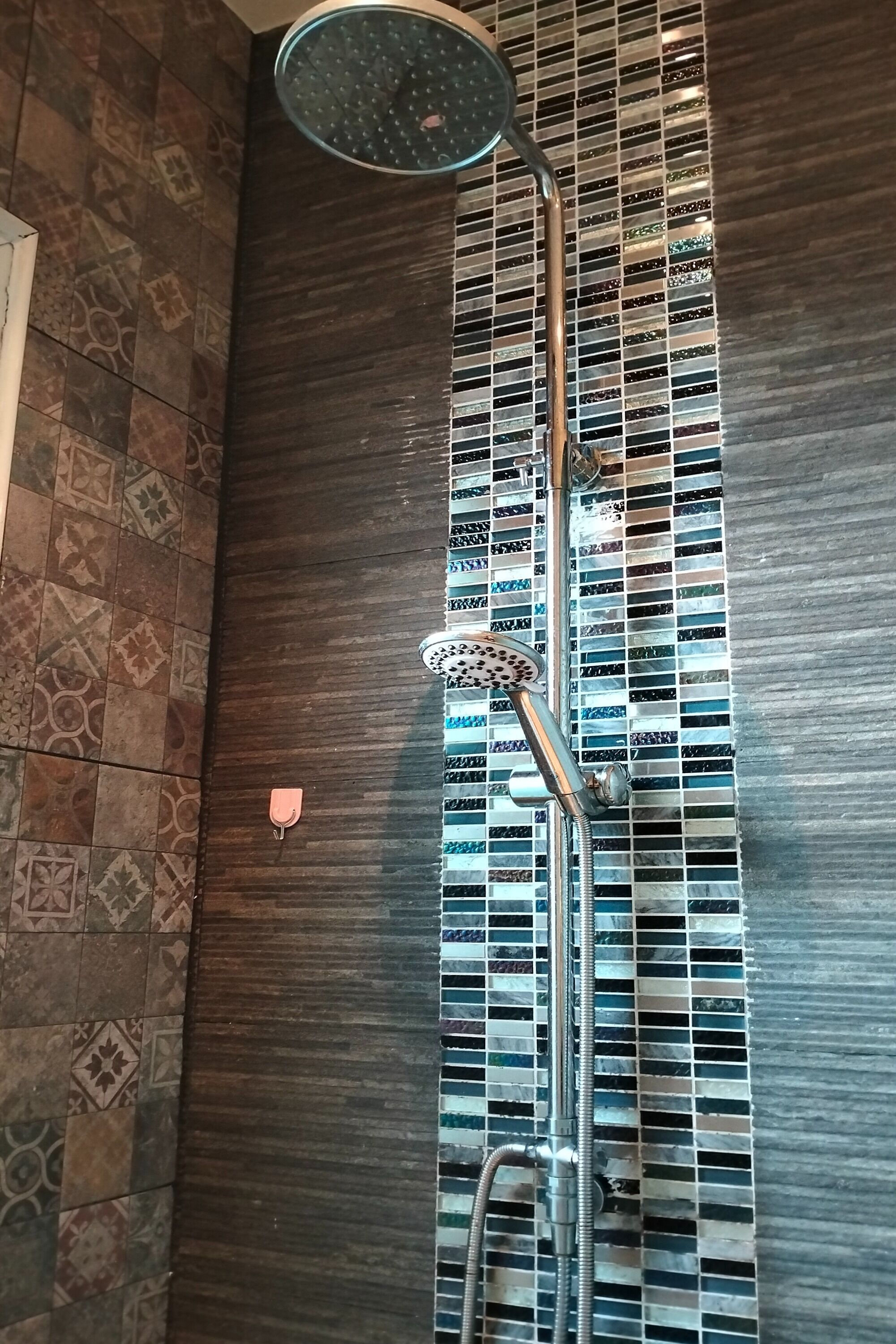 A shower with a rain showerhead and a handheld showerhead, set against a wall with a patterned tile design.