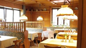Un restaurante con muebles de madera, manteles blancos y lámparas colgantes.