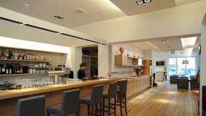 A modern bar area with a wooden counter, bar stools, and shelves stocked with bottles and glasses. - Baurs Park (Hamburg)