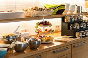 A buffet setup with various food items, including fruits, breads, and condiments.