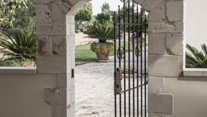 Une entrée en arc de pierre surmontée d’un portail en métal, qui mène à un chemin pavé bordé de verdure.