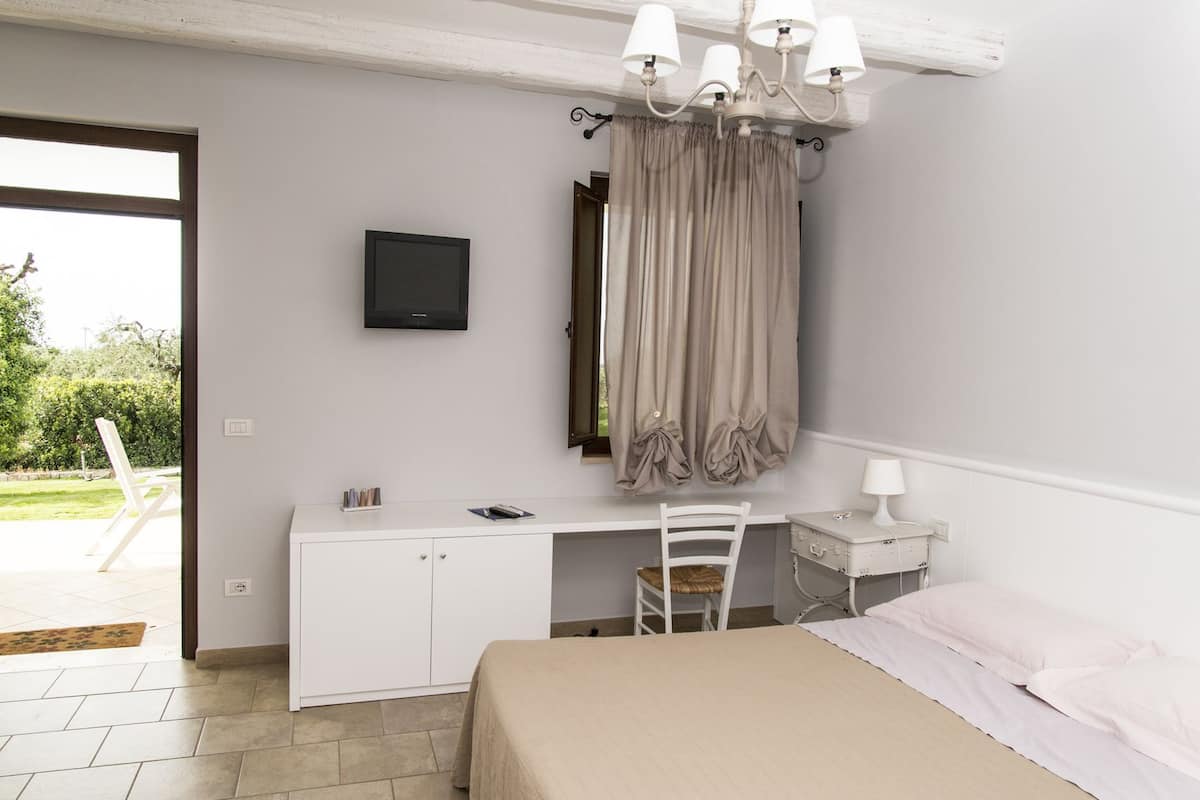 Een slaapkamer met een bed, bureau, stoel, televisie en een raam met gordijnen.