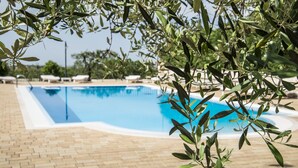 A swimming pool with a tiled deck and lounge chairs in the background. - Masseria Gravelle (Conversano)