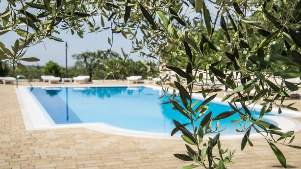 Une piscine avec une terrasse carrelée et des chaises longues à l’arrière-plan.